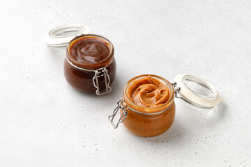 Liquid melted caramel syrup, paste in round glass jars with lid isolated on a gray background....