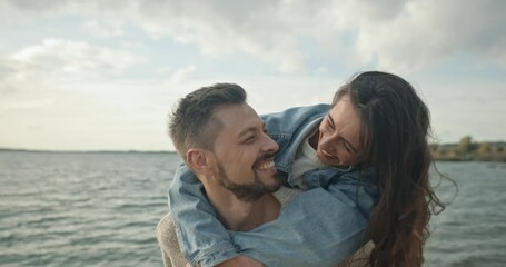 Portrait of young playful happy couple of beautiful cheerful bearded man and cute joyful woman on back of husband smiling laughing. Upbeat husband and wife playing around near lake. - Powered by Adobe