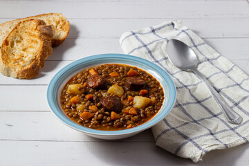 Traditional lentil soup with legs, carrots and chorizo on a white and blue plate on a white background. Mediterranean cuisine.