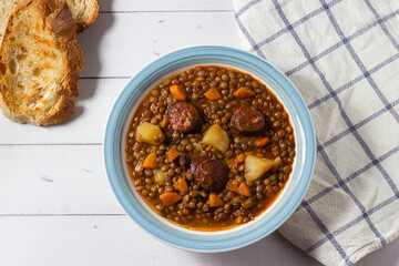 Traditional lentil soup with legs, carrots and chorizo on a white and blue plate on a white background. Mediterranean cuisine.