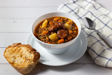 Traditional lentil soup with legs, carrots and chorizo on a white on a white background. Mediterranean cuisine.