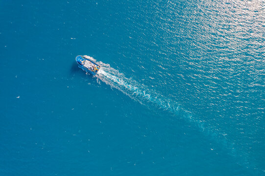 Small cargo ship sails through blue sea to serve fish farm, aerial top view