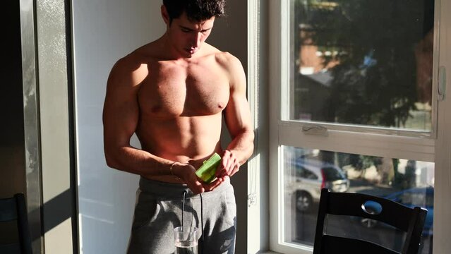 Muscular shirtless young man taking pills at home