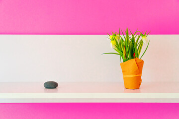Small flowers in the pot wrapped paper and oval stone on white shelf wood. Pink wall background with copy space for text. 