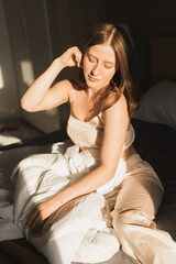Obraz premium Girl portrait is waking up in morning stretches in bed and sun shines from window. Happy young woman greets new sunny day