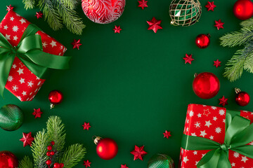 Christmas mood concept. Flat lay photo of red present boxes with green bows, Christmas baubles pine branches on deep green background with copy space in the middle.