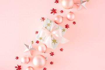 New Year concept. Flat lay photo of present box with bow pink Christmas baubles star ornaments on pastel pink background with copy space. Creative holiday card idea.