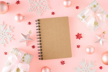 New Year concept. Top view composition of present boxes with bows and Christmas baubles star ornaments white snowflakes on pastel pink background with card note. Creative holiday card idea.