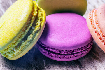 Close-up of multicolored traditional French macaroons laying on wooden background board, festive almond cookie design