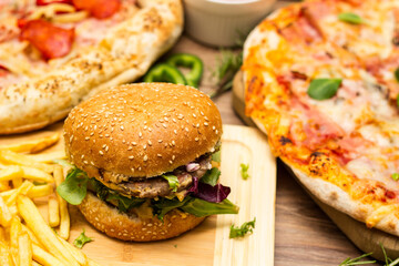 Pepperoni pizza and pizza Capricciosa with mozzarella cheese, ham, tomato sauce, salami, mushroom, pepper, spices and fresh basil. Hamburger with fries and fresh salad. On wooden table background