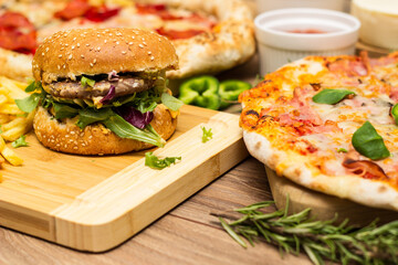 Pepperoni pizza and pizza Capricciosa with mozzarella cheese, ham, tomato sauce, salami, mushroom, pepper, spices and fresh basil. Hamburger with fries and fresh salad. On wooden table background