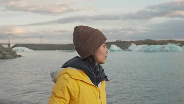 Beautiful young asian woman in yellow jacket enjoy walking on the beach in the evening among the iceberg floating in Jokulsarlon