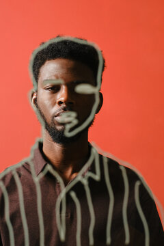 Vertical through glass with lining drawing portrait shot of stylish young Black man standing against coral wall background looking at camera