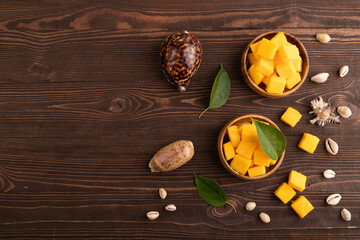 Dried mango cubes in wooden bowls on brown wooden, top view, copy space.