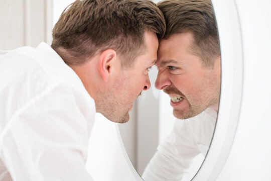 Caucasian man being angry on himself screaming on his reflection on the mirror