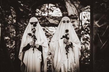 A funny image of two people with black roses in ghost costumes and sunglasses in an abandoned...