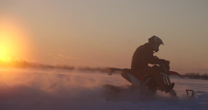 Man riding snowmobile dirtbike conversion on winter day at sunset - speeds past setting sun
