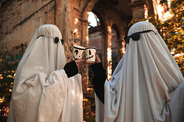 A funny image of two people in ghost costumes and sunglasses holding a cup with a drink in an...