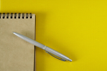 A spring-loaded notepad made from eco-friendly recycled paper and a silver fountain pen lie on a yellow textured anti-stress surface. Copy space.