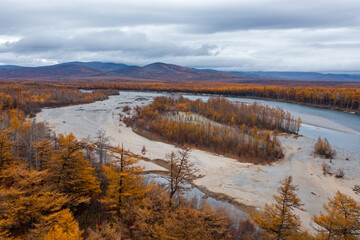 Fototapeta premium Autumn aerial view of the river valley. Top view of the river and forest. Mountains in the distance. Northern nature. Travel to Siberia and the Russian Far East. Ola river, Magadan Region, Russia.