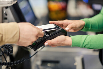 Close up of the cashier holding pos terminal while man is holding credit card at checkout. - obrazy, fototapety, plakaty