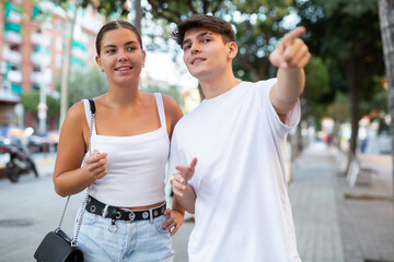 Young couple walking outdoors together, making pointing finger gesture.