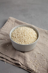 Raw Organic Carnaroli Rice in a Bowl on a gray surface, side view.