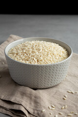 Raw Organic Carnaroli Rice in a Bowl on a gray surface, side view.