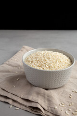 Raw Organic Carnaroli Rice in a Bowl on a gray surface, side view.