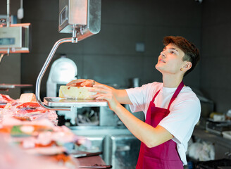 Young salesman weighing cheese on a scale in a grocery store - Powered by Adobe