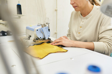 Concentrated seamstress hemming piece of bright yellow fabric using serger sewing machine