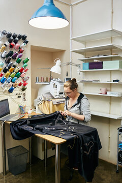 Vertical shot of young woman embroidering beautiful pattern on dark fabric
