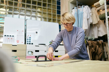 Mature Caucasian woman working in tailor workshop transferring pattern onto fabric 