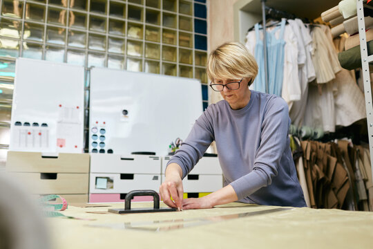 Mature Caucasian Woman Working In Tailor Workshop Transferring Pattern Onto Fabric 