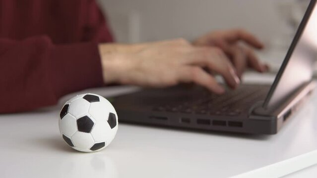 Young man reading soccer news or writing football article on laptop. Soccer ball on the table. Betting, gambling concept.