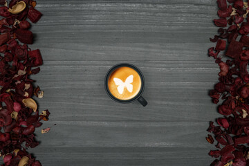Gray wooden background with coffee cup, milk foam and decoration red leaves on the sides