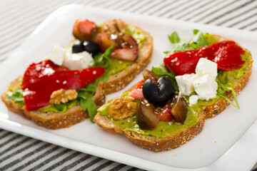 Fototapeta na wymiar Slices of bread with guacamole and soft cheese decorated with fresh vegetables, herbs and walnut.