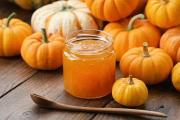 Jar of healthy pumpkin jam and wooden spoon. Pumpkins on kitchen table.