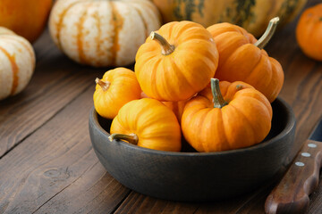 Several small pumpkins in a wooden bowl on a kitchen table.