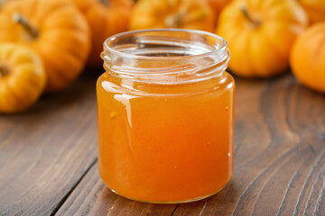 Jar of healthy pumpkin jam on kitchen table. Pumpkins in the background.