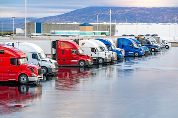 Different big rig semi trucks with semi trailers standing on the truck stop parking lot at early...