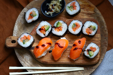Sushi and rolls with avocado and salmon on a wooden board.