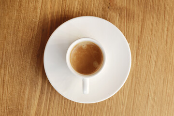 Top view of white porcelain cup with plate of hot coffee with milk on wooden table background.