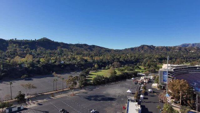 Panning aerial footage the Rose Bowl Stadium surrounded by lush green palm trees and majestic mountain ranges with blue sky and clouds in Pasadena California USA