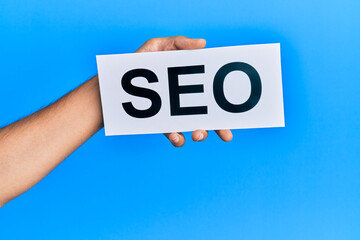 Hand of caucasian man holding paper with seo word over isolated blue background