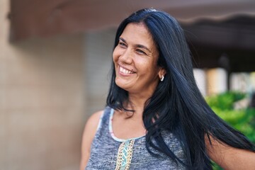 Middle age hispanic woman smiling confident looking to the side at street