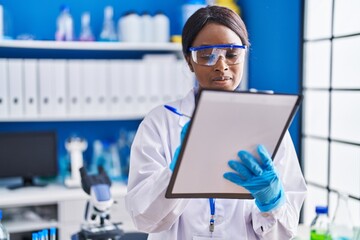 Young african american woman scientist writing on document at laboratory