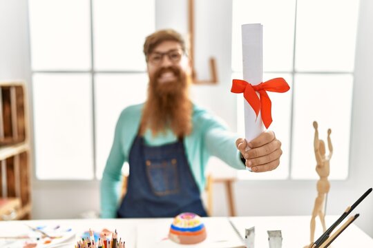 Young redhead man smiling confident holding diploma at art studio