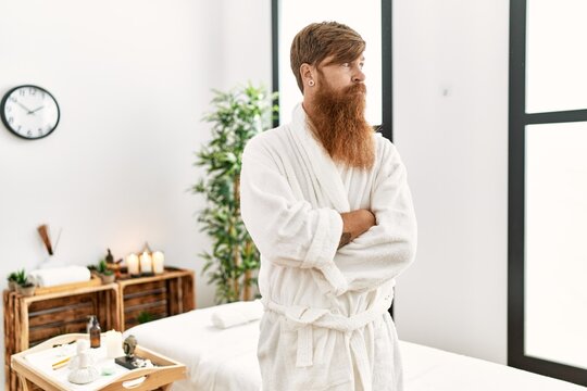 Redhead man with long beard wearing bathrobe at wellness spa looking to side, relax profile pose with natural face with confident smile.