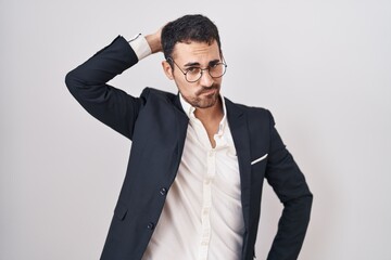 Handsome business hispanic man standing over white background confuse and wondering about question. uncertain with doubt, thinking with hand on head. pensive concept.